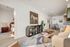 Modern open-concept living room with stylish decor, featuring a cozy sofa, abstract artwork, and a view into a warmly lit bedroom.