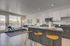 Modern open-concept kitchen and living area featuring sleek cabinetry, stylish bar stools, and floor-to-ceiling windows offering abundant natural light.