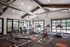 Modern fitness center with high ceilings, featuring red exercise bikes, treadmills, and weight benches in a bright and airy space.