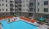 Modern apartment complex featuring a sparkling blue swimming pool with bright orange lounge chairs and stylish balconies.