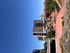 Modern apartment building under a clear blue sky, surrounded by unique red rock landscapes and lush greenery.