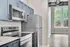 Contemporary kitchen with sleek stainless steel appliances and vibrant blue cabinetry, leading to a bright living space with a large window view.