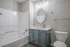 Modern bathroom with elegant bathtub, sleek vanity, and stylish gray cabinets, complemented by a large oval mirror and contemporary lighting.