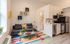 Charming living area with a cozy gray sofa, vibrant multicolor rug, and a modern kitchenette. Stylish shelving and bright decor create a welcoming ambiance.
