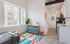 Chic urban studio with large windows, vibrant decor, and open kitchen layout.