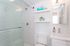 Modern bathroom featuring a sleek glass shower, chic white tile walls, and elegant shelving with stylish decor.