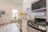 Modern and bright apartment kitchen featuring sleek stainless steel appliances, white cabinetry, and a stylish backsplash with natural light streaming in through a window.