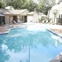 Inviting apartment complex pool area with sparkling water, surrounded by lush trees and comfortable lounge chairs.