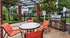Charming outdoor patio with vibrant orange chairs and a stainless steel grill, nestled under a rustic pergola in a lush garden setting.