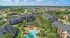 Vibrant aerial view of a charming apartment complex with lush greenery, a sparkling pool, and spacious walking paths set against a suburban landscape.