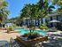 Inviting outdoor pool area with lush greenery, modern seating, and umbrella-shaded tables, perfect for relaxation and socializing.