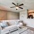 Elegant living room with plush sofa, decorative pillows, glass coffee table with flowers, and a ceiling fan, showcasing cozy and inviting interior design.
