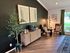 Charming living room corner with elegant decor, featuring plush armchairs, a sleek wooden cabinet, and artistic wall frames, offering a warm and inviting atmosphere.