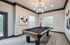 Elegant game room featuring a sleek billiard table beneath a modern chandelier, with artistic wall decorations and large windows offering natural light.