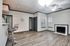 Modern apartment interior with sleek grey flooring, elegant bar seating, and a cozy fireplace. Natural light fills the space, highlighting stylish features and a ceiling fan.