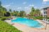 Lush apartment pool area with sun loungers, palm trees, and tranquil ambiance on a sunny day.