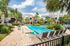 Luxurious apartment complex with a sparkling outdoor pool surrounded by lush palm trees and modern lounge chairs under sunny skies.