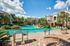 Luxurious apartment complex with a sparkling pool surrounded by lush palm trees and stylish outdoor seating, perfect for relaxation and leisure.