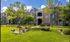 Charming apartment complex surrounded by lush greenery, featuring a communal outdoor space with seating and barbecue area.