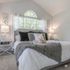 Chic and cozy bedroom with vaulted ceiling, featuring elegant decor, plush bedding, and abundant natural light through an arched window.