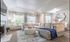 Elegant living room with a plush sectional sofa, stylish tufted ottoman, and ambient natural light filtering through large windows.