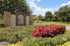 Charming entrance to The Trails at Corinthian Creek, with lush landscaping and vibrant flower beds under a clear blue sky.