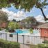 Charming apartment complex featuring a beautifully landscaped pool area with sun loungers, vibrant greenery, and stunning architecture under a bright blue sky.