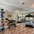 Modern apartment fitness center with mirrored walls, featuring a treadmill, vibrant medicine balls, and a set of free weights on sleek hardwood flooring.