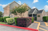 Charming brick apartment exterior with lush landscaping, vibrant plants, and clear blue sky, highlighting a welcoming entrance to the leasing center.