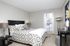 Elegant bedroom with chic gray decor, soft lighting, and large window offering natural sunlight.