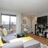Bright and cozy living room with modern decor, featuring a comfortable gray sofa, vibrant yellow accents, and a sleek wall-mounted TV, leading to a private balcony.