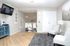 Bright and welcoming living area with modern decor, featuring elegant gray chairs, a stylish lamp, and a contemporary wall-mounted TV. Hardwood floors lead to a cozy dining space with natural light streaming in through large windows.