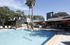 Inviting outdoor pool area with elegant sun loungers and vibrant orange umbrellas, surrounded by lush greenery and modern architecture.