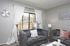 Chic living room with plush gray sofas, stylish wall art, and a large window offering natural light and a view of a cozy patio.