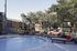 Inviting outdoor pool area with elegant lounge chairs and vibrant red cushions, surrounded by lush greenery and modern apartment buildings.