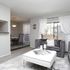 Elegant living space with plush gray sofas, chic white decor, natural light from large windows, and a cozy dining area.