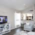 Bright and cozy living room with modern decor, featuring a plush armchair, wall-mounted TV, and a view into a sleek kitchen with stylish bar stools.