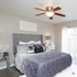 Bright and elegant bedroom showcasing a plush gray bed, decorative pillows, mirrored nightstands, and a modern ceiling fan, with natural light streaming through large sliding doors.