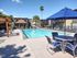 Inviting apartment complex courtyard featuring a sparkling swimming pool, comfortable lounge chairs, and vibrant blue umbrellas under a clear sky.