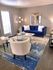 Chic living room with plush blue sofa, elegant white accent chairs, modern floor lamp, and stylish decor on a textured blue area rug.