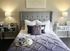 Elegant bedroom with a plush grey headboard, luxurious pillows, and stylish decor, including mirrored nightstands and ambient lighting.
