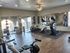 Bright and modern gym with state-of-the-art equipment, featuring exercise bikes, a weight rack, and large mirrors in a spacious workout area with wooden flooring and natural light.