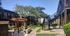 Charming apartment complex with well-maintained greenery, a wooden pergola, and inviting outdoor seating under clear blue skies.