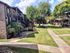 Charming apartment complex with lush landscaping, mature trees, and inviting outdoor paths under a bright blue sky.