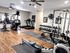 Modern gym equipped with a variety of fitness machines and free weights on sleek wooden flooring, illuminated by ceiling fans.