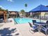 Inviting apartment complex featuring a crystal-clear swimming pool, elegant lounge chairs, and shaded outdoor seating under blue umbrellas.