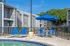 Charming apartment complex with modern gray exteriors, featuring a refreshing swimming pool area with blue sun loungers and a stylish umbrella.