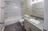 Elegant bathroom with modern fixtures, featuring a sleek granite countertop, tiled shower with curved rod, and stylish wood-look flooring.