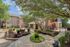 Charming apartment courtyard featuring lush greenery, vibrant flowers, and inviting seating areas under the shade of large trees.