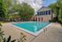 Inviting outdoor pool area with sun loungers, lush greenery, and a charming clubhouse backdrop.